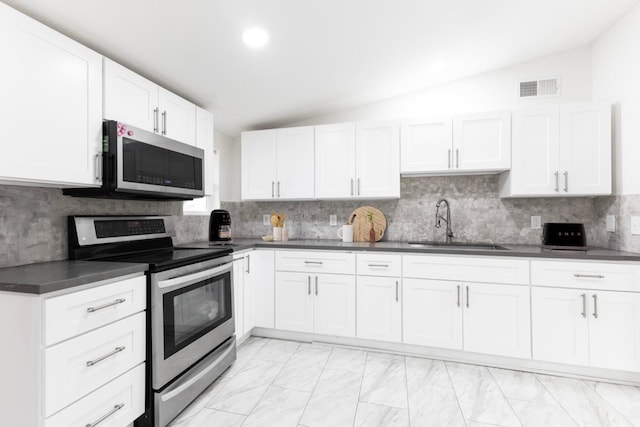 kitchen featuring lofted ceiling, stainless steel appliances, a sink, marble finish floor, and dark countertops