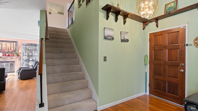 foyer entrance with wood-type flooring, a notable chandelier, and a brick fireplace