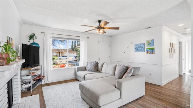 living room featuring hardwood / wood-style floors, ceiling fan, a textured ceiling, and a brick fireplace