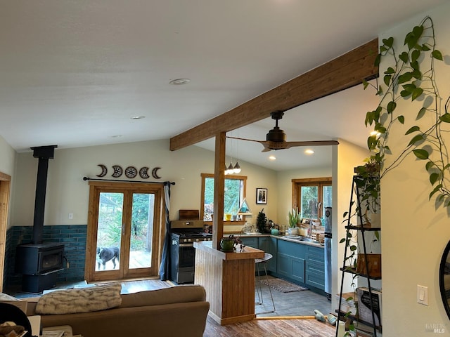 interior space featuring blue cabinetry, vaulted ceiling with beams, a wood stove, light hardwood / wood-style flooring, and gas range