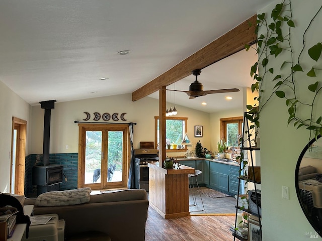 living room featuring sink, a wood stove, ceiling fan, hardwood / wood-style floors, and lofted ceiling with beams