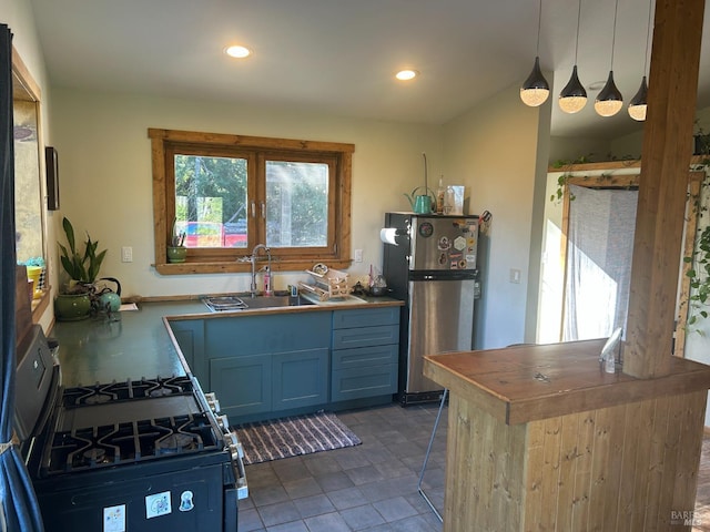 kitchen featuring blue cabinetry, range with gas cooktop, stainless steel fridge, sink, and decorative light fixtures