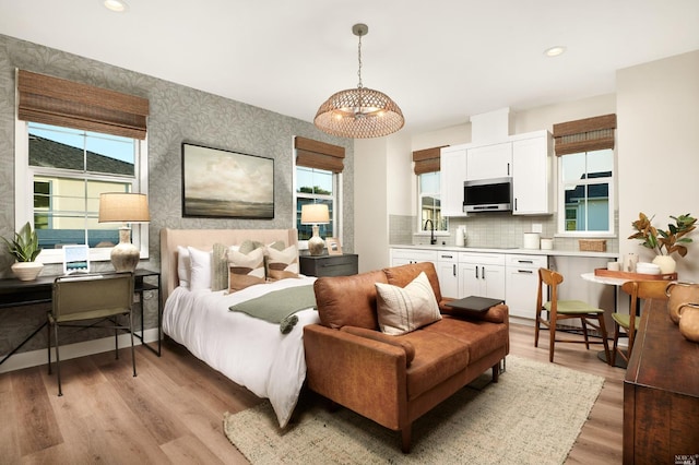 bedroom with light hardwood / wood-style floors, an inviting chandelier, and sink