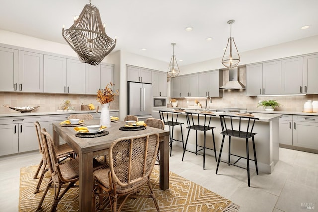 kitchen with a kitchen island with sink, wall chimney range hood, decorative backsplash, gray cabinets, and high end fridge