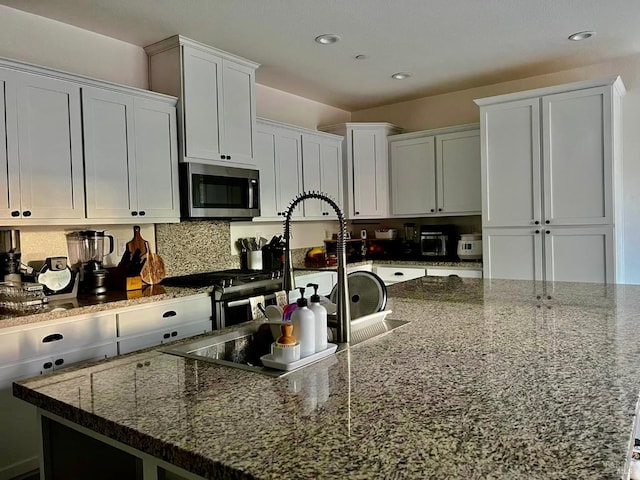 kitchen with a kitchen island with sink, dark stone countertops, decorative backsplash, and white cabinetry