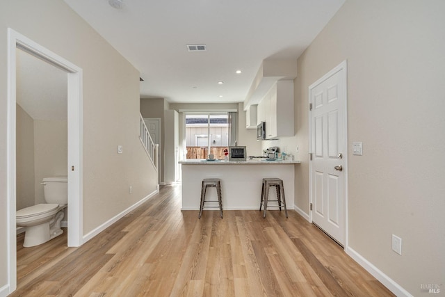 kitchen featuring white cabinetry, light hardwood / wood-style flooring, kitchen peninsula, and a breakfast bar