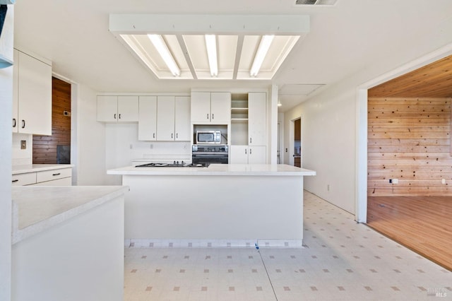 kitchen with kitchen peninsula, wood walls, black gas stovetop, oven, and white cabinets