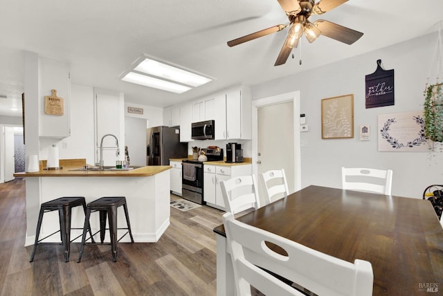 kitchen with appliances with stainless steel finishes, sink, a breakfast bar area, white cabinets, and dark wood-type flooring