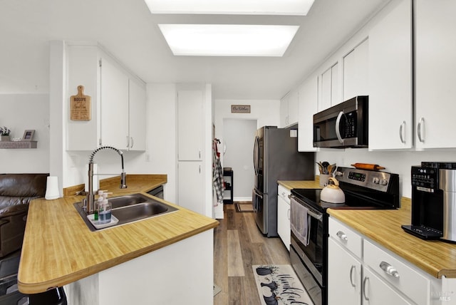 kitchen with appliances with stainless steel finishes, white cabinetry, sink, kitchen peninsula, and light wood-type flooring