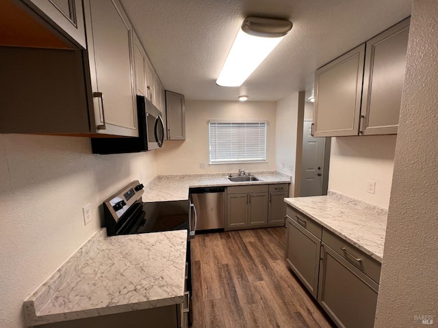 kitchen with sink, dark wood-type flooring, a textured ceiling, gray cabinets, and appliances with stainless steel finishes