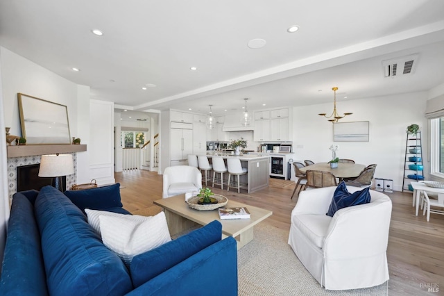 living room with light hardwood / wood-style flooring, a chandelier, and wine cooler