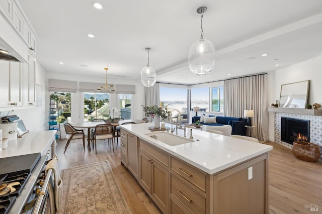 kitchen with an island with sink, high end range, pendant lighting, a tile fireplace, and sink