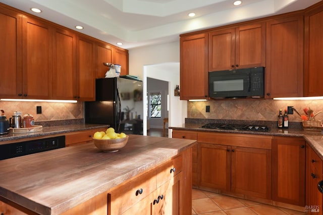 kitchen featuring wood counters, tasteful backsplash, a raised ceiling, black appliances, and light tile patterned floors