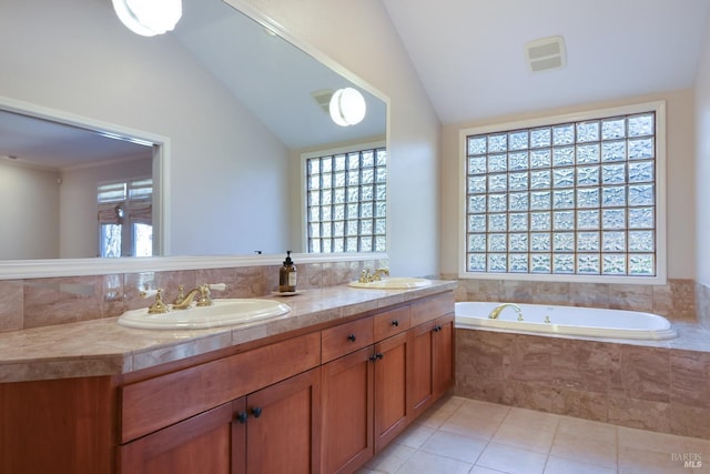 bathroom featuring tile patterned flooring, vanity, tiled bath, and vaulted ceiling