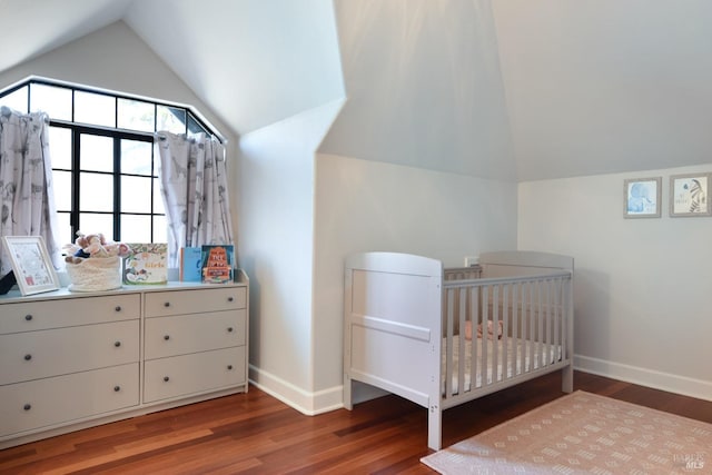 unfurnished bedroom featuring a crib, dark hardwood / wood-style flooring, and vaulted ceiling