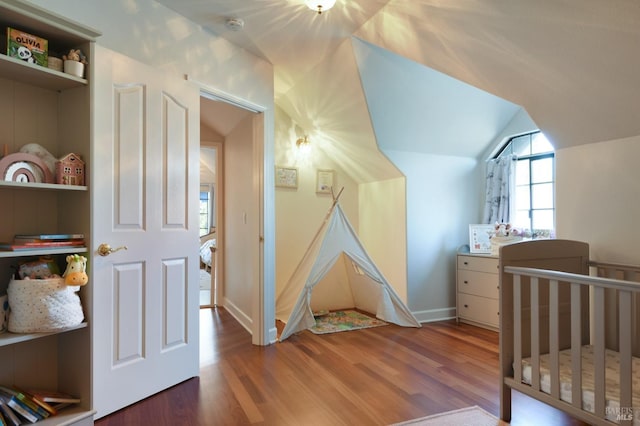 bedroom featuring hardwood / wood-style flooring, vaulted ceiling, and a nursery area