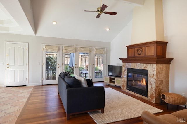 tiled living room featuring ceiling fan, a fireplace, high vaulted ceiling, and french doors