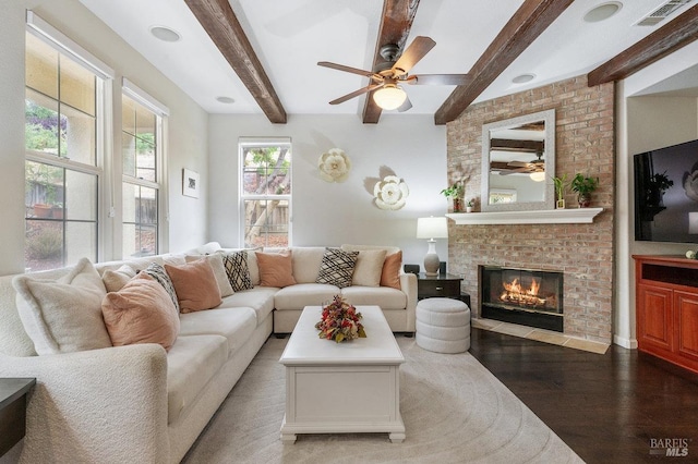 living area featuring a ceiling fan, visible vents, a brick fireplace, beam ceiling, and wood finished floors