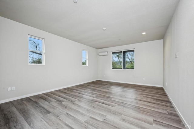 unfurnished room with a wall mounted AC and light hardwood / wood-style floors