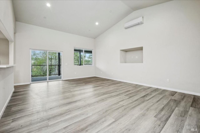 unfurnished room with an AC wall unit, high vaulted ceiling, and light wood-type flooring