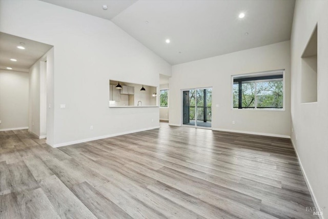 unfurnished living room featuring high vaulted ceiling and light hardwood / wood-style floors