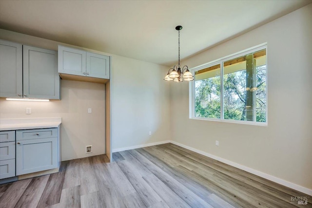 kitchen with gray cabinetry, a notable chandelier, decorative light fixtures, and light hardwood / wood-style flooring