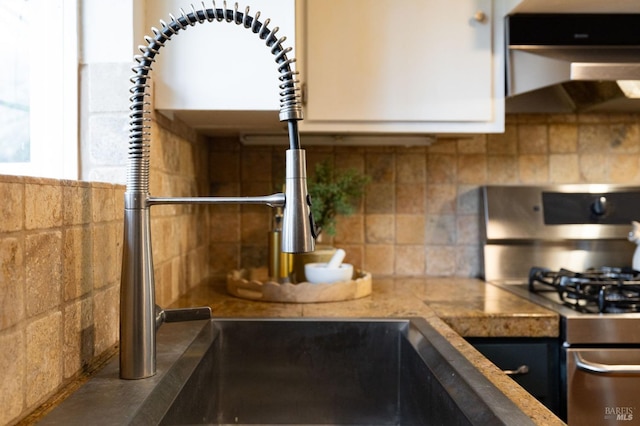 kitchen with a sink, under cabinet range hood, backsplash, and stainless steel range with gas stovetop