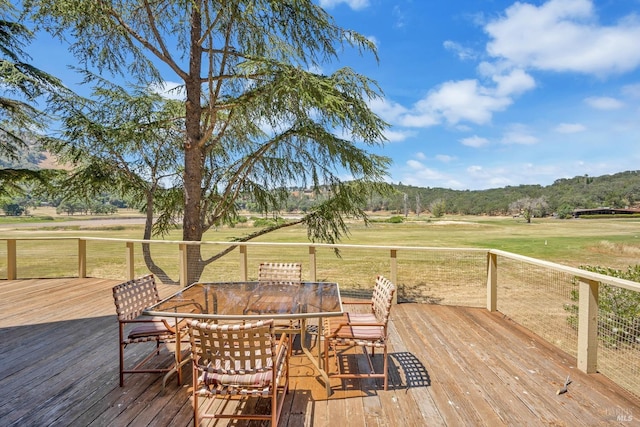 wooden deck with outdoor dining space, a lawn, and a rural view