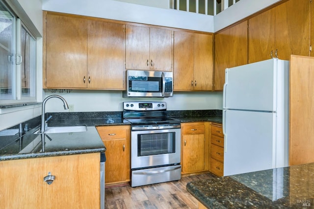 kitchen featuring dark stone counters, sink, light wood-type flooring, and appliances with stainless steel finishes