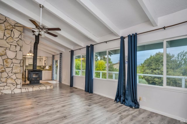 unfurnished living room featuring a wood stove, vaulted ceiling with beams, ceiling fan, light wood-type flooring, and a textured ceiling