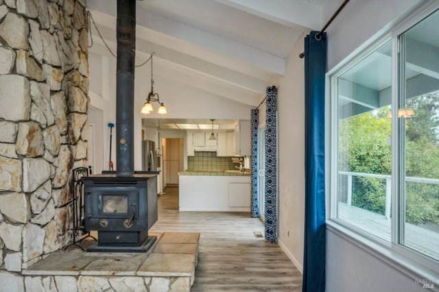 unfurnished living room with a wood stove, light wood-type flooring, and vaulted ceiling with beams