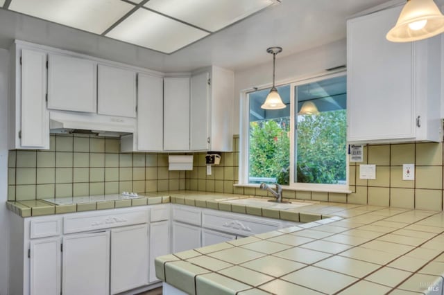 kitchen with decorative light fixtures, tile countertops, white cabinetry, and tasteful backsplash