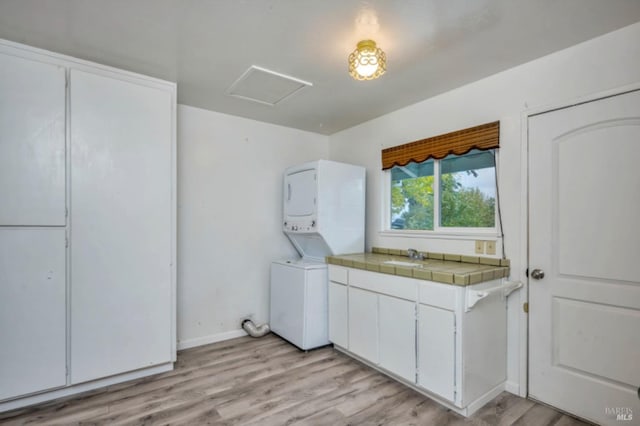 clothes washing area with stacked washer / drying machine, cabinets, light wood-type flooring, and sink