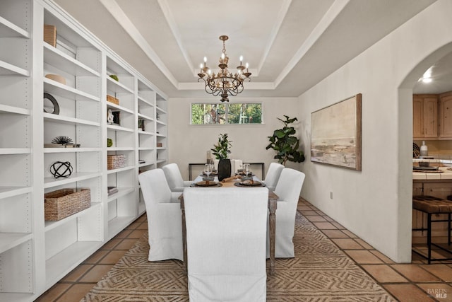 dining area with dark tile patterned floors, an inviting chandelier, and a tray ceiling