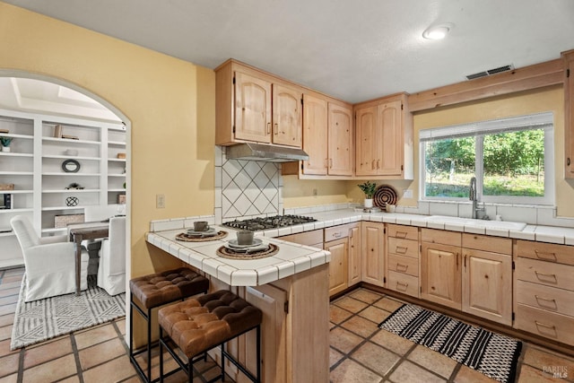 kitchen featuring stainless steel gas cooktop, sink, light brown cabinets, tile counters, and backsplash