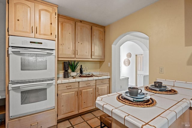 kitchen featuring light brown cabinets, tile counters, double oven, and light tile patterned floors