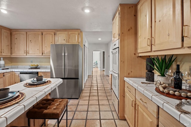 kitchen featuring stainless steel appliances, tile countertops, and light brown cabinetry