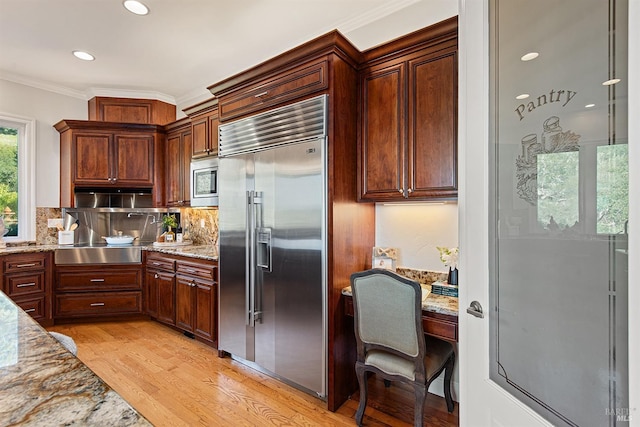 kitchen with decorative backsplash, crown molding, built in appliances, light hardwood / wood-style flooring, and light stone counters