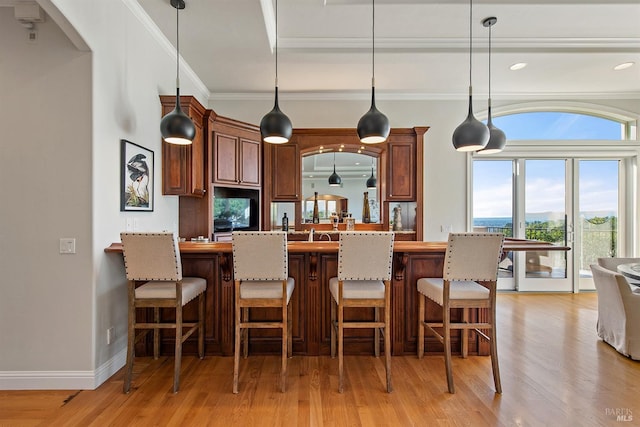 kitchen with pendant lighting, light hardwood / wood-style flooring, ornamental molding, and a breakfast bar area