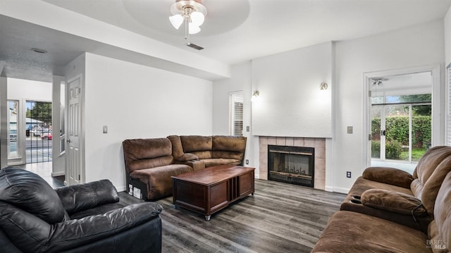 living room featuring ceiling fan, a healthy amount of sunlight, dark wood-type flooring, and a tiled fireplace