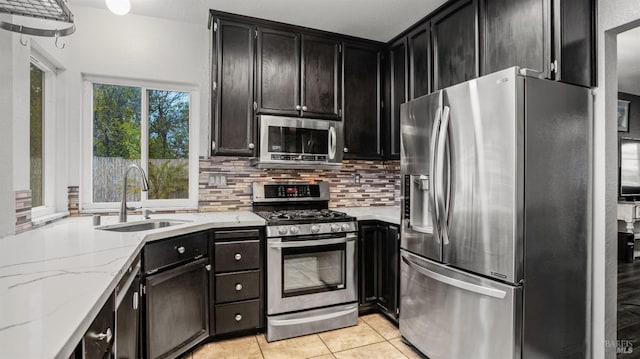 kitchen with sink, tasteful backsplash, light stone counters, light tile patterned floors, and appliances with stainless steel finishes