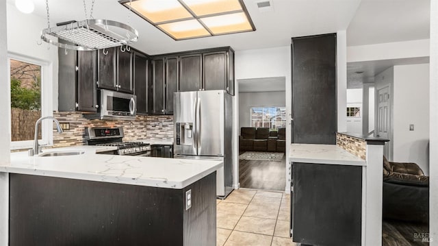 kitchen featuring sink, kitchen peninsula, dark brown cabinets, light tile patterned floors, and appliances with stainless steel finishes