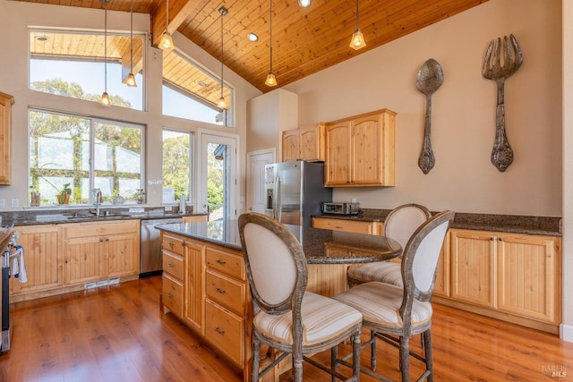 kitchen featuring light brown cabinets, light wood-style flooring, stainless steel appliances, a sink, and beamed ceiling