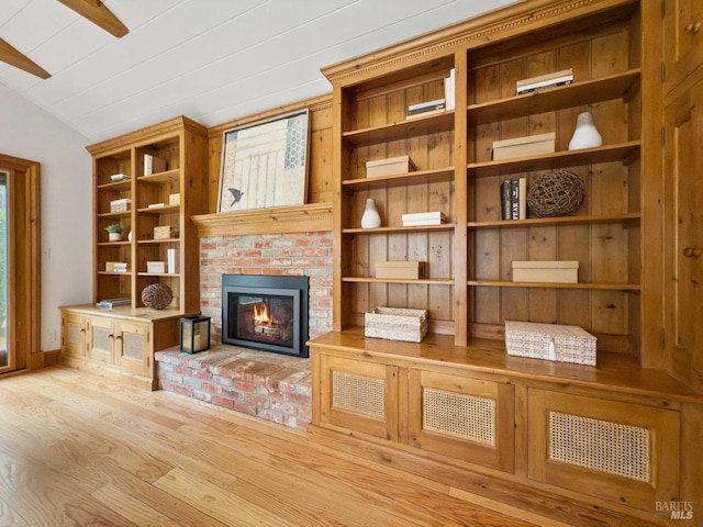 unfurnished living room featuring vaulted ceiling, plenty of natural light, light hardwood / wood-style floors, and a brick fireplace