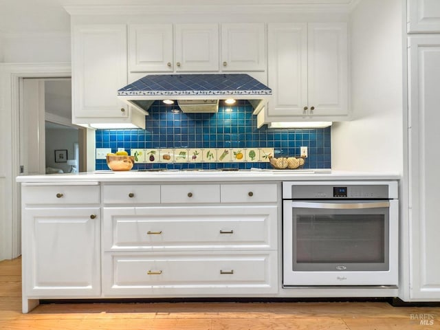 kitchen featuring premium range hood, stainless steel oven, white cabinetry, and backsplash