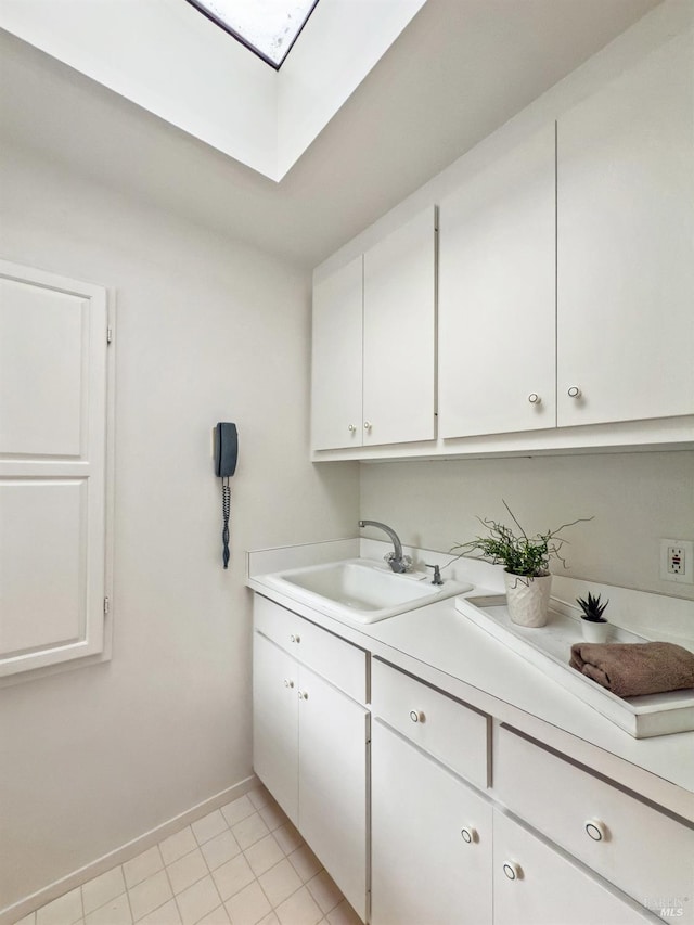 clothes washing area with sink, a skylight, and light tile patterned flooring