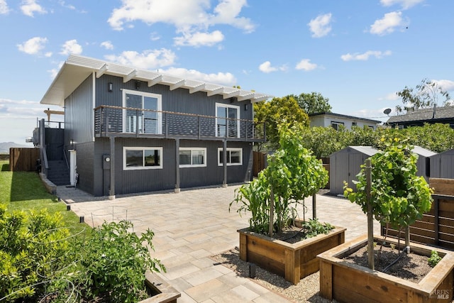 back of property with a balcony, a patio, and a storage shed