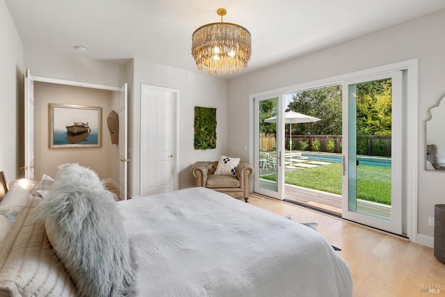 bedroom featuring access to exterior, light wood-type flooring, and an inviting chandelier