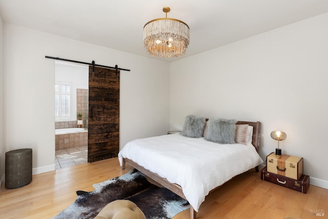 bedroom featuring a barn door, a chandelier, ensuite bath, and wood-type flooring