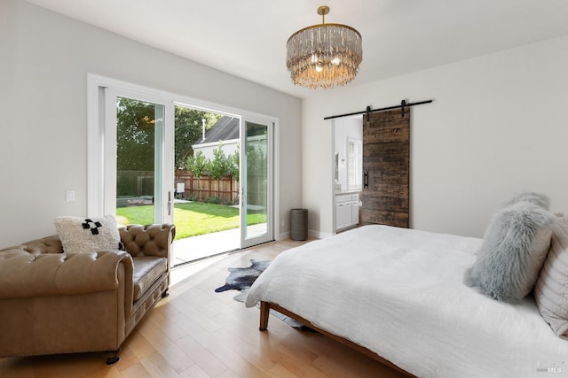 bedroom with a barn door, access to exterior, light wood-type flooring, and an inviting chandelier